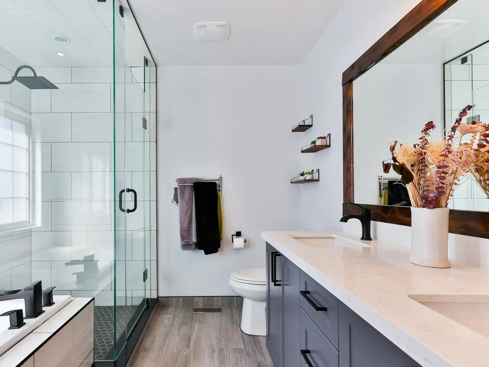 Remodeled bathroom with a glass shower, toilet and a long double vanity with black faucets